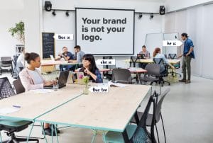 a group of people sitting at tables in an office with a sign that says your brand is not your logo