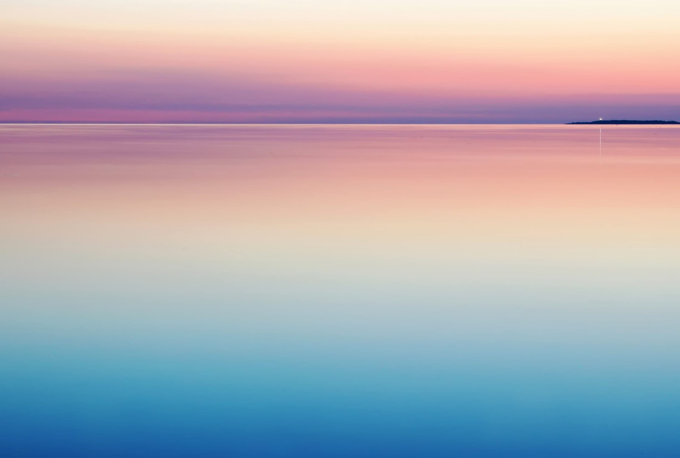 a sunset over the ocean with a small island in the distance