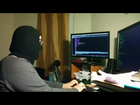 a man wearing a mask is typing on a keyboard in front of two computer monitors