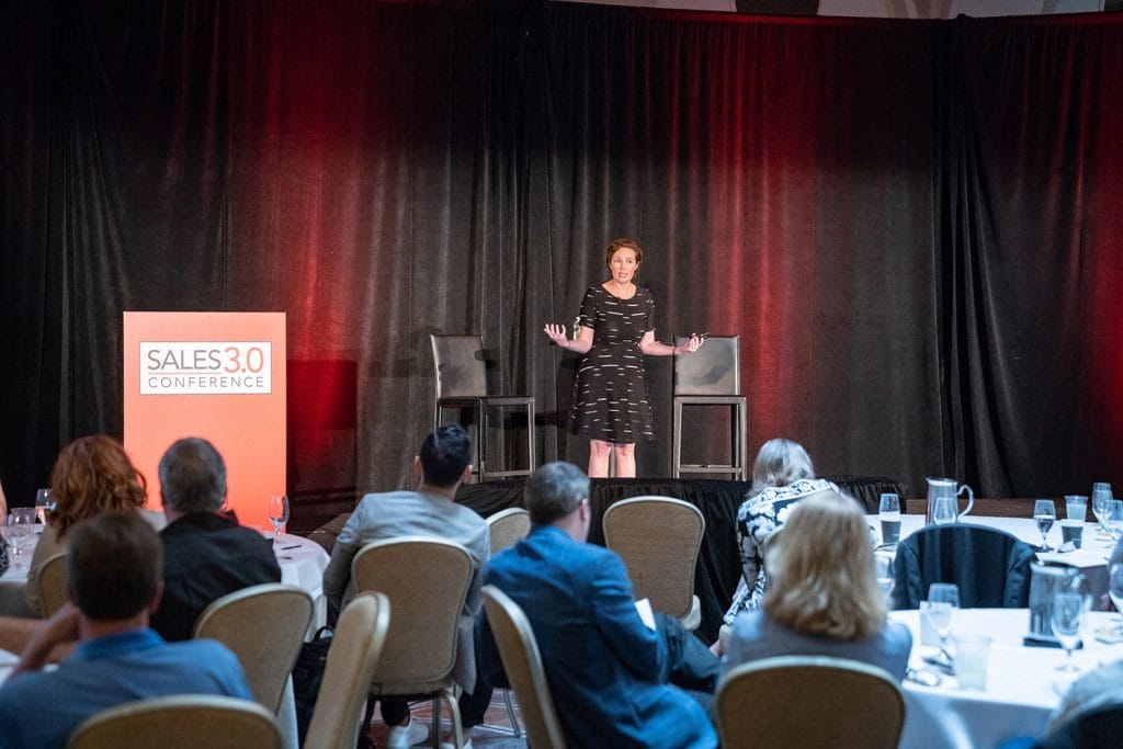 a woman stands on a stage at a sales 3.0 conference