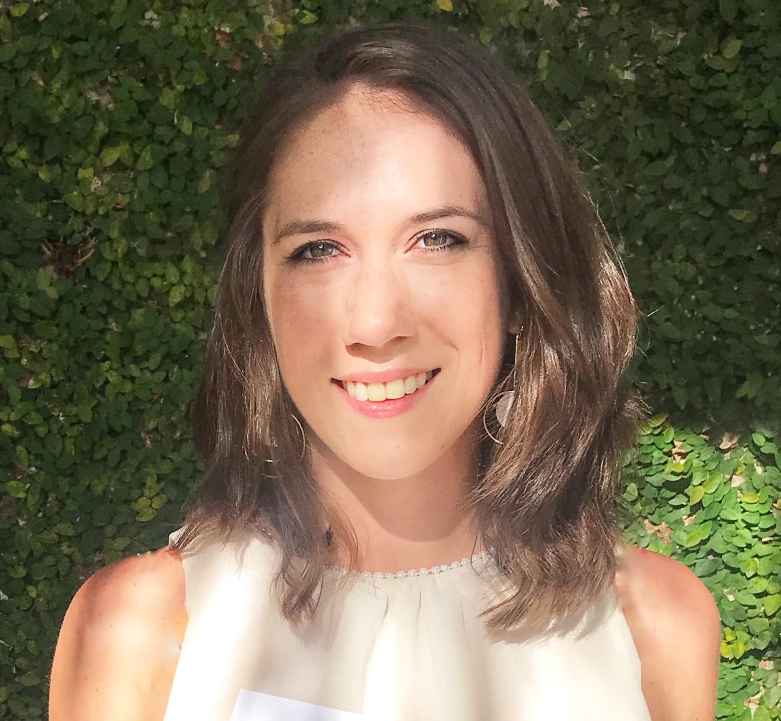 a woman in a white top smiles in front of a green wall