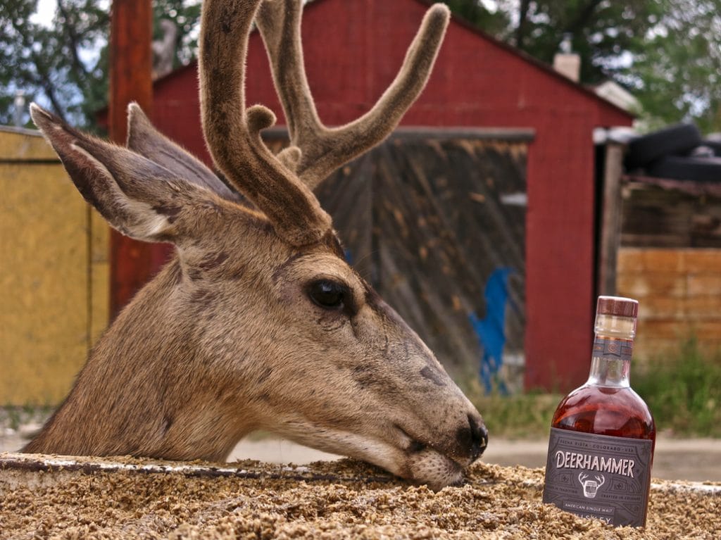 a deer standing next to a bottle of deerhammer whiskey