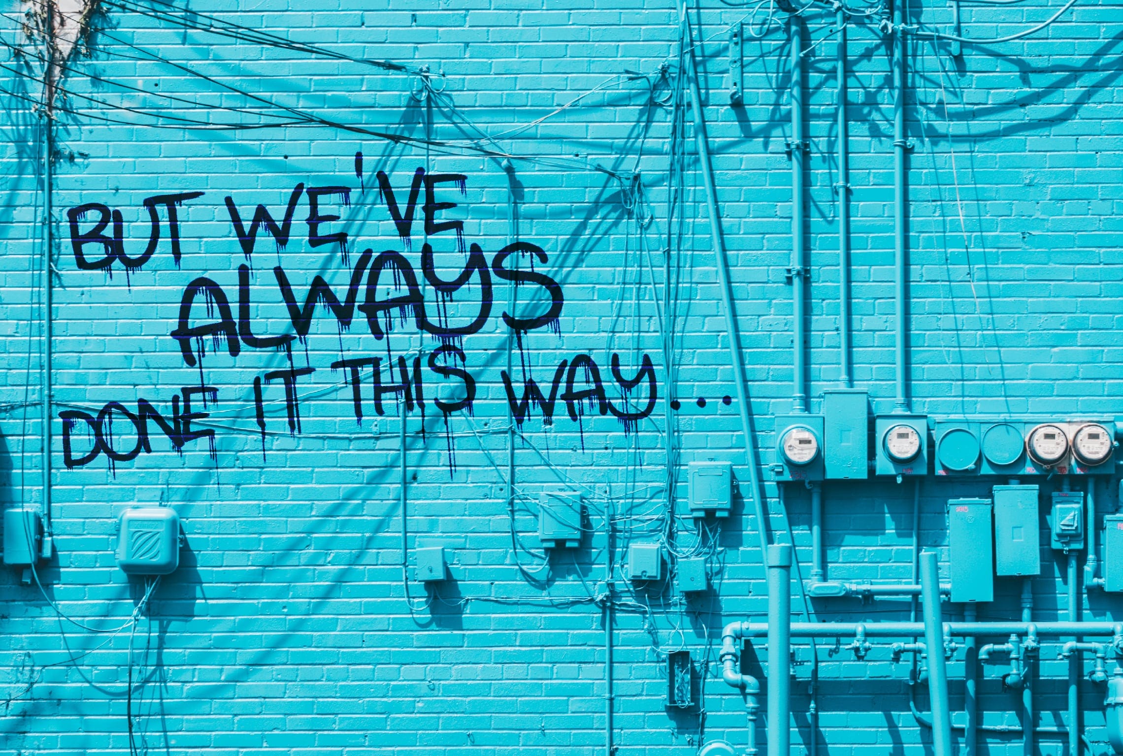 a blue brick wall with graffiti that says but we've always done it this way