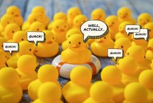 yellow rubber ducks with speech bubbles that say quack and one speech bubble above the middle duck that says well actually