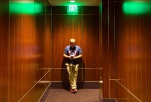a man standing in a hallway with a green exit sign above him