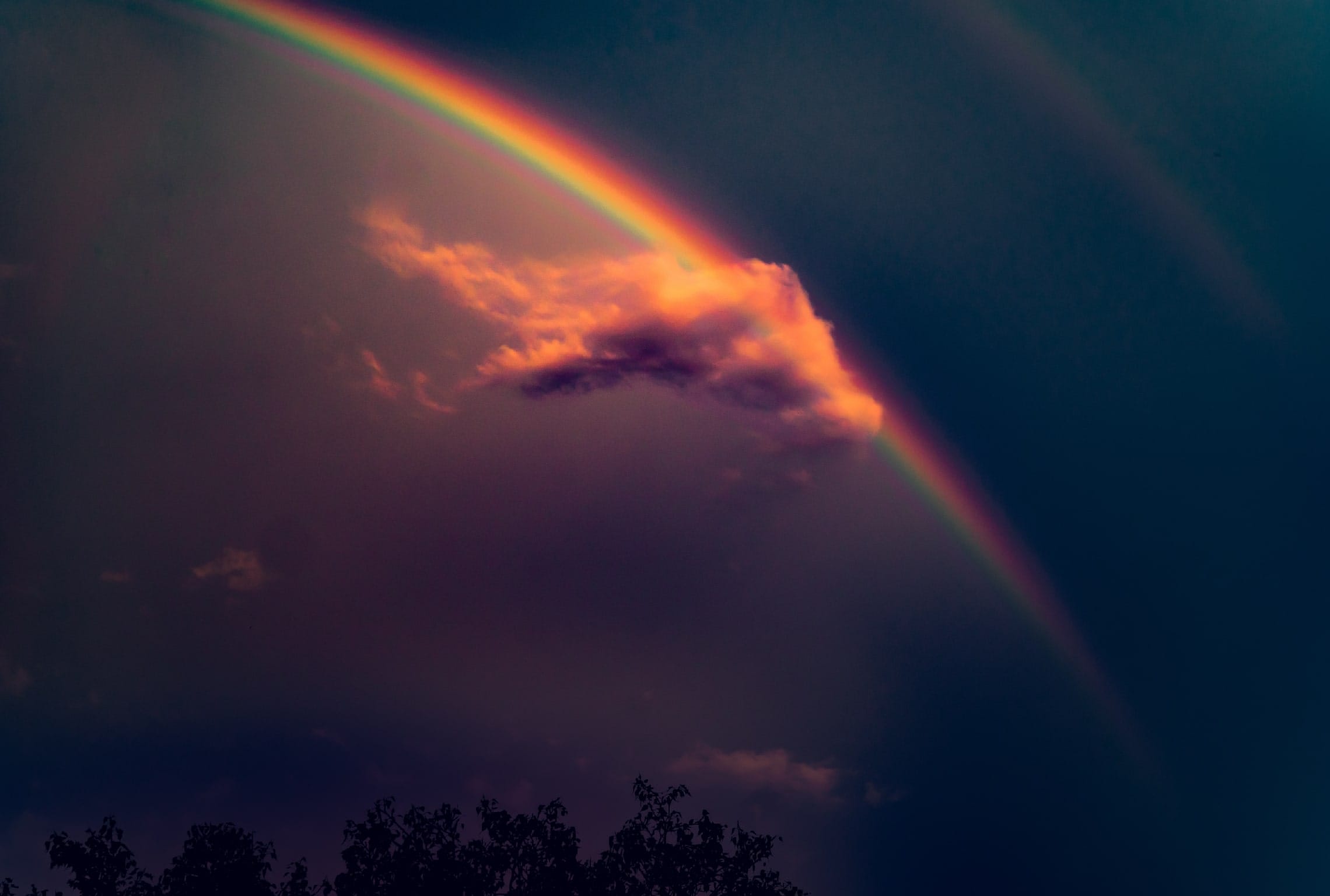 a rainbow is visible behind a cloud in a dark sky