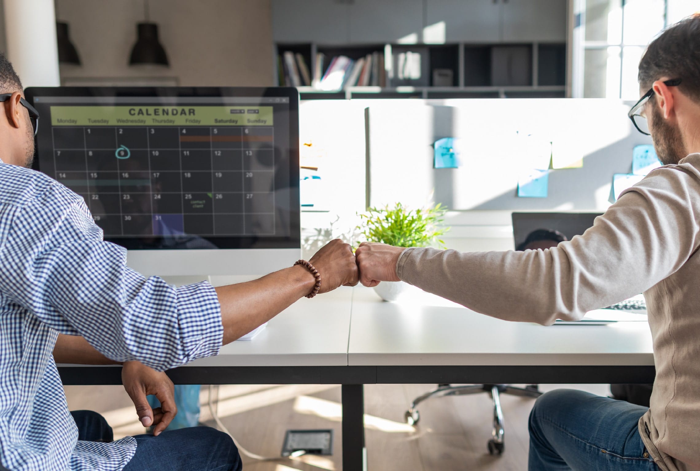 two men at a desk giving each other a fist bump