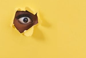 a woman's eye is peeking through a hole in a yellow wall