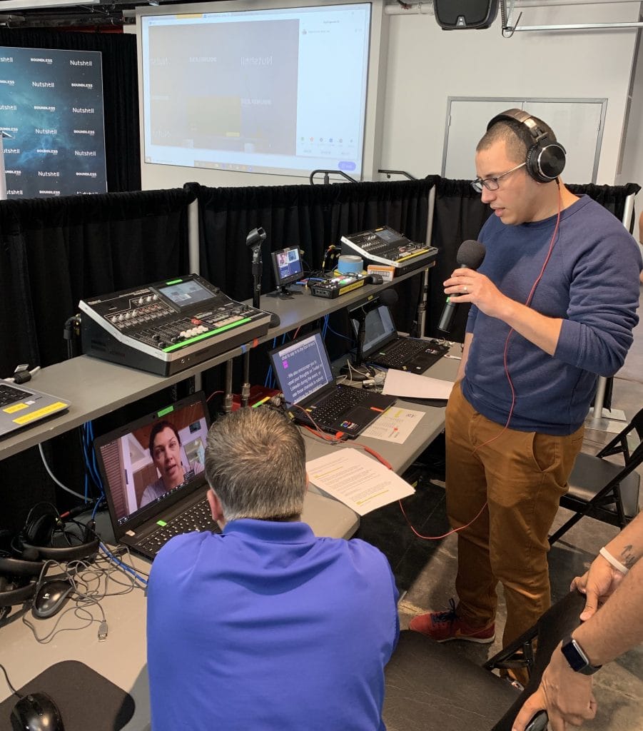 ben godlstein wearing headphones is talking into a microphone while another man watches