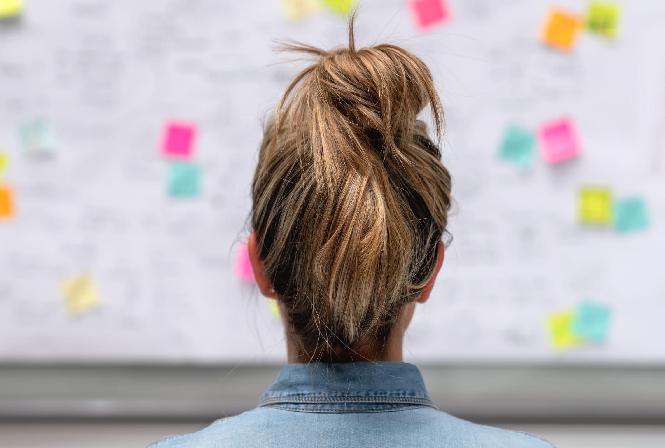 a woman in a ponytail looks at sticky notes on a board