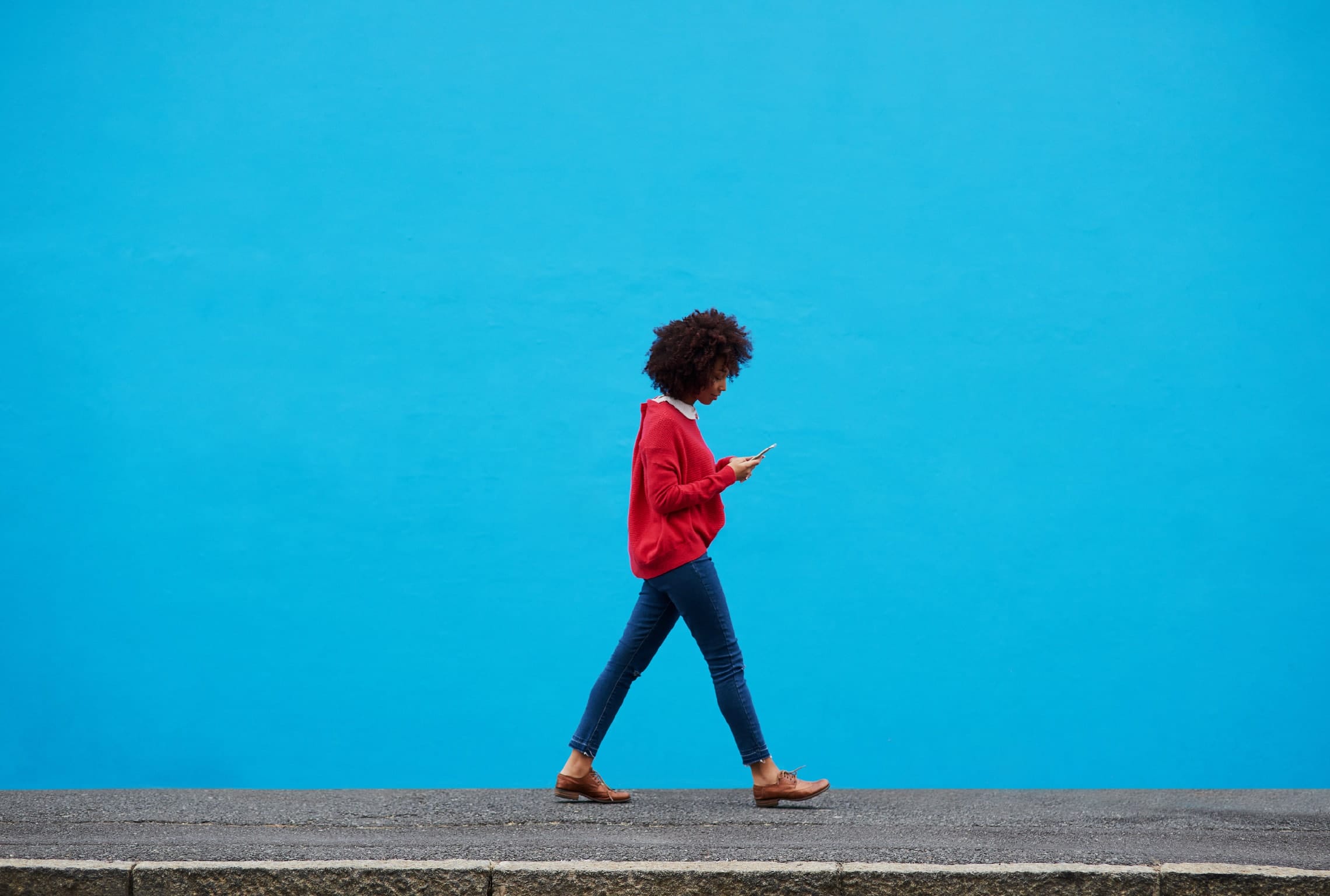 a woman in a red sweater is walking down a sidewalk and looking at her phone