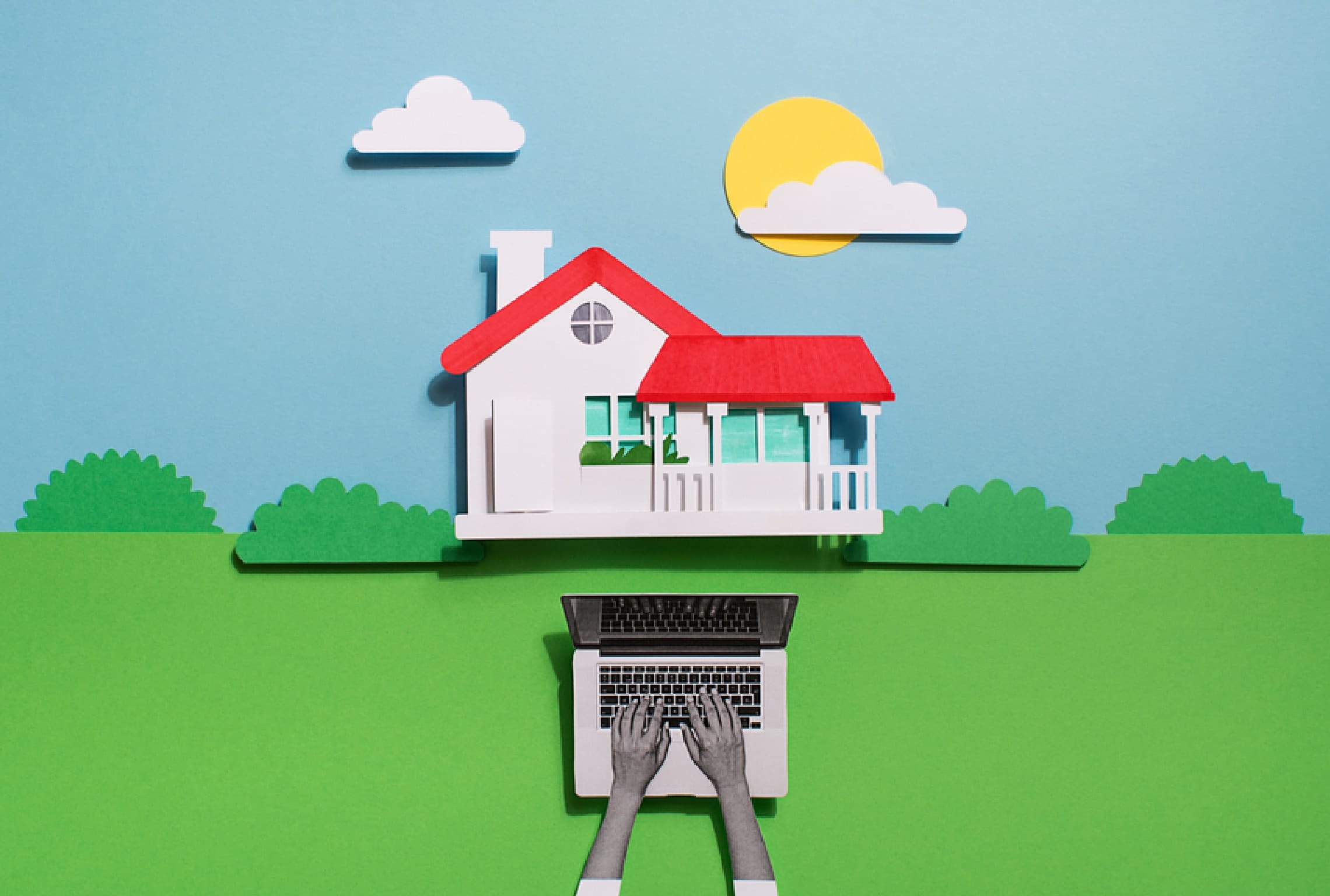 a person is typing on a laptop in front of a paper house