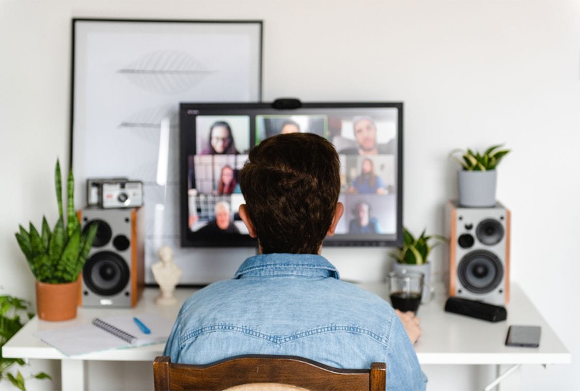 a man sits at a desk looking at a computer screen with a group of people on it