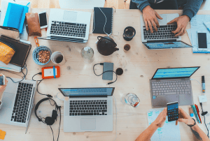 a group of people are sitting at a table with laptops and phones