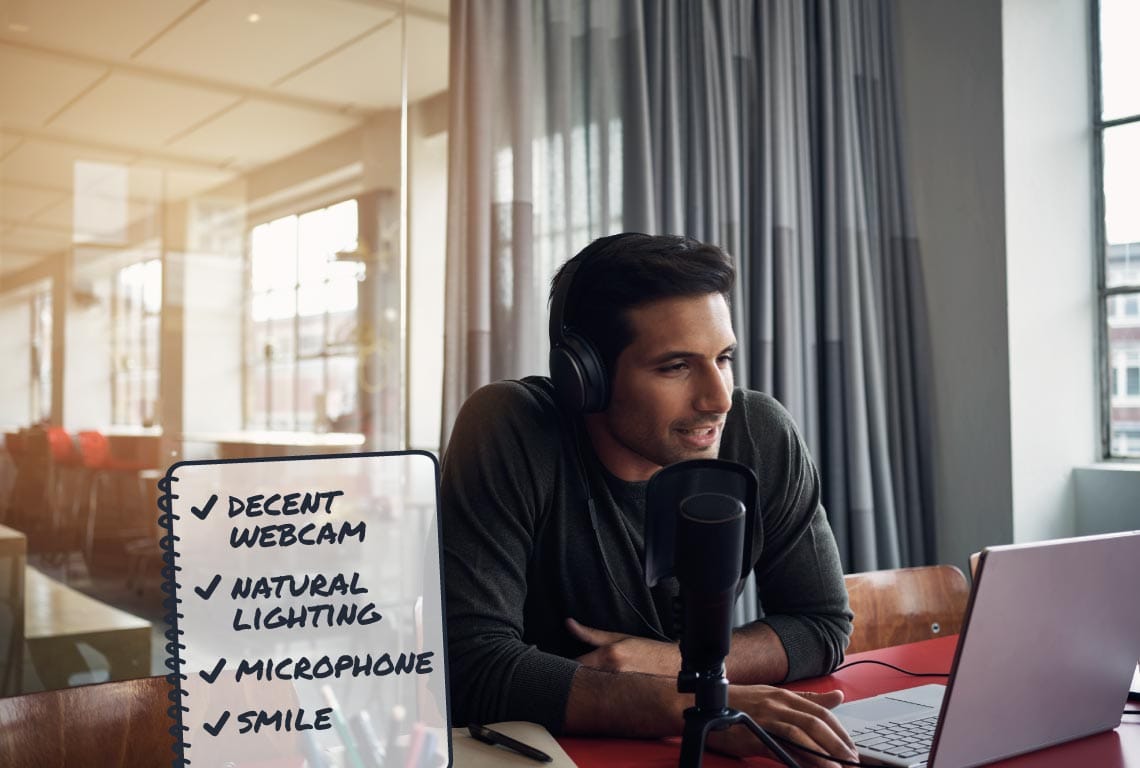 a man wearing headphones sits at a desk with a laptop and a notepad with a checklist for videos next to him