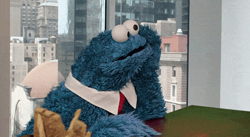 a cookie monster sitting at a table with a city in the background