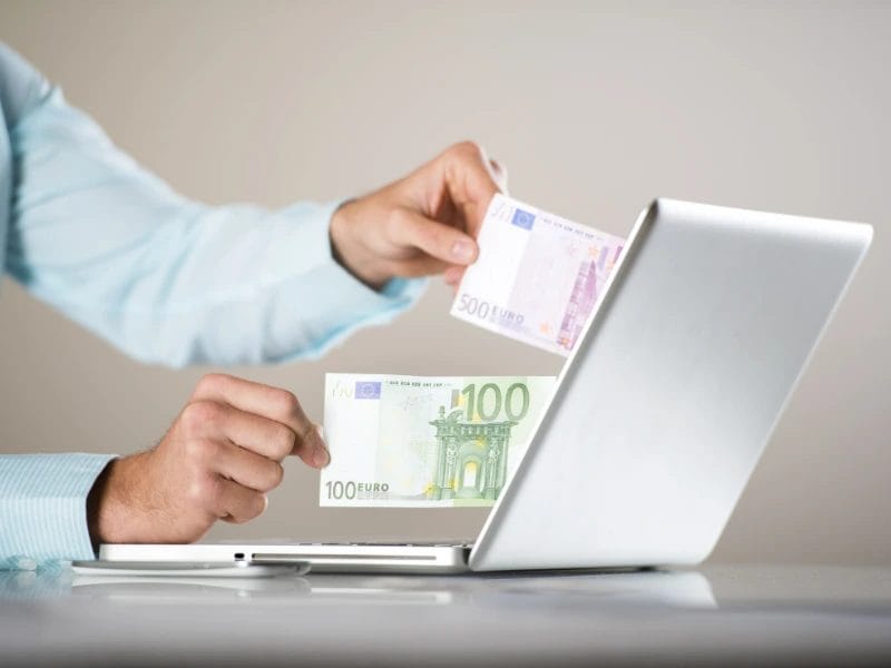 uma pessoa segurando uma nota de 100 euros na frente de um laptop