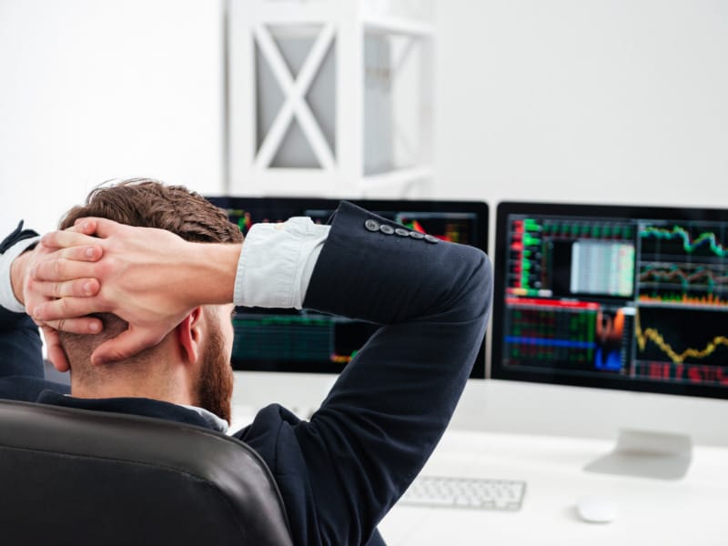 un homme assis devant deux écrans d'ordinateur, les mains derrière la tête