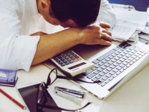 a man rests his head on a calculator next to a laptop