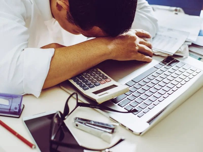a man rests his head on a calculator next to a laptop