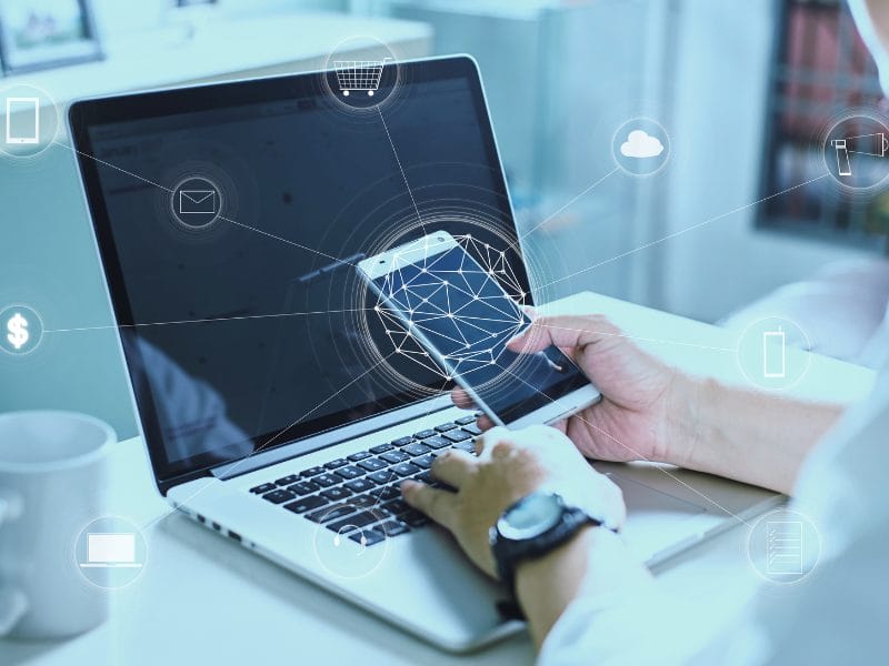 a person is using a laptop and holding a cell phone