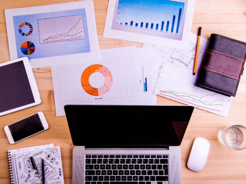 a laptop is open on a wooden desk surrounded by papers and graphs