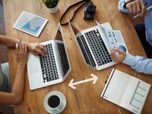 a man and a woman are sitting at a table using laptops