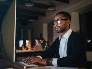 a man wearing glasses is typing on a computer keyboard