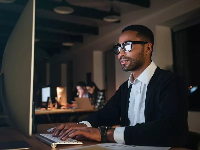 a man wearing glasses is typing on a computer keyboard