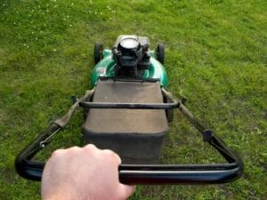 a person is pushing a green lawn mower in the grass