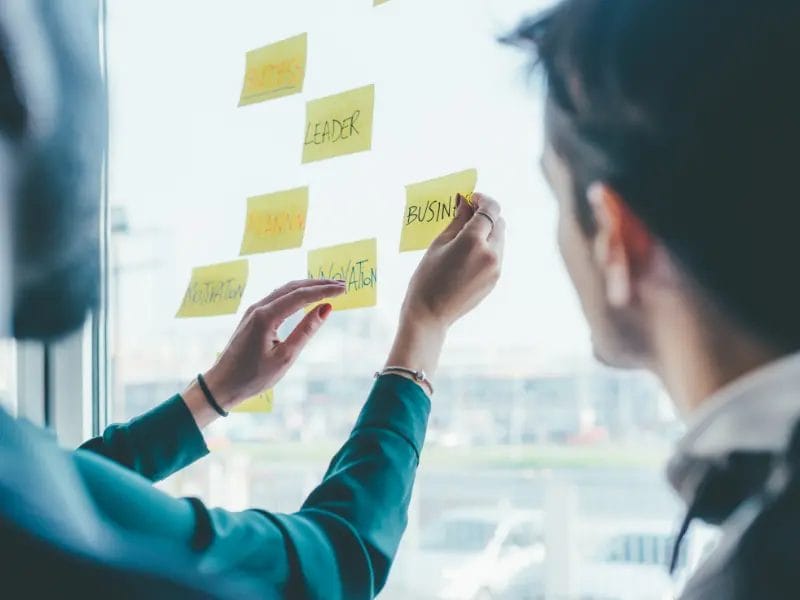 a man and a woman are writing on sticky notes on a window
