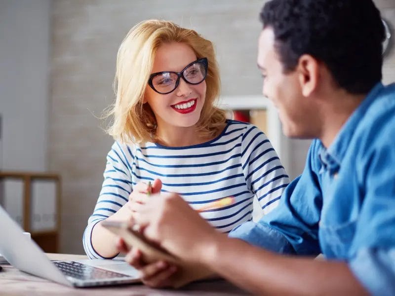 two people talking to each other in front of a laptop