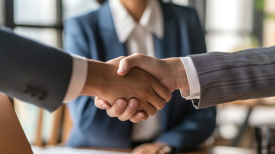 two persons in suits shaking hands while a lady is in front of them